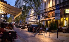 PURO - Lodź - Letní večer poblíž Piotrkowska. Rušná dlážděná ulice, listnaté stromy, kavárny, hospody, restaurace a zahrady mezi půvabnými činžáky.